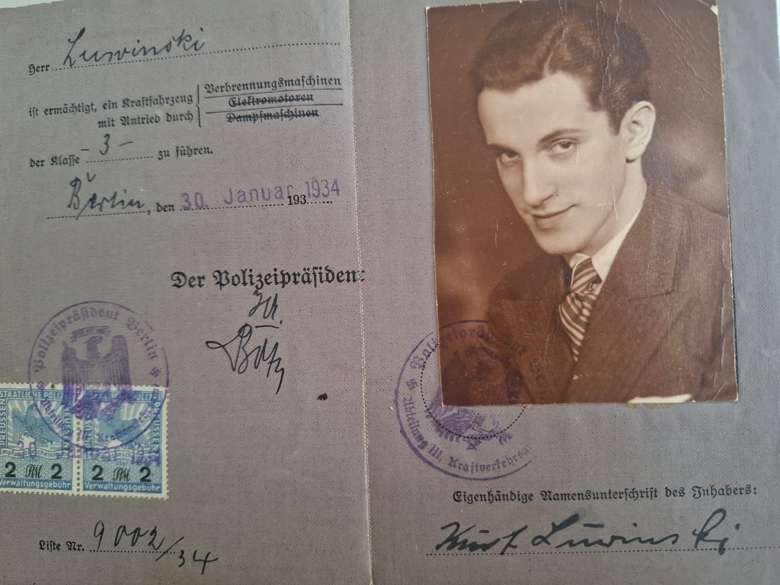 The inner spread of Kurt Luwinski's 1934 Berlin driving licence: a photograph of him at twenty-one, his own signature, two two-Mark Prussian fee stamps, and the Police President's stamp and signature dated 30 January 1934